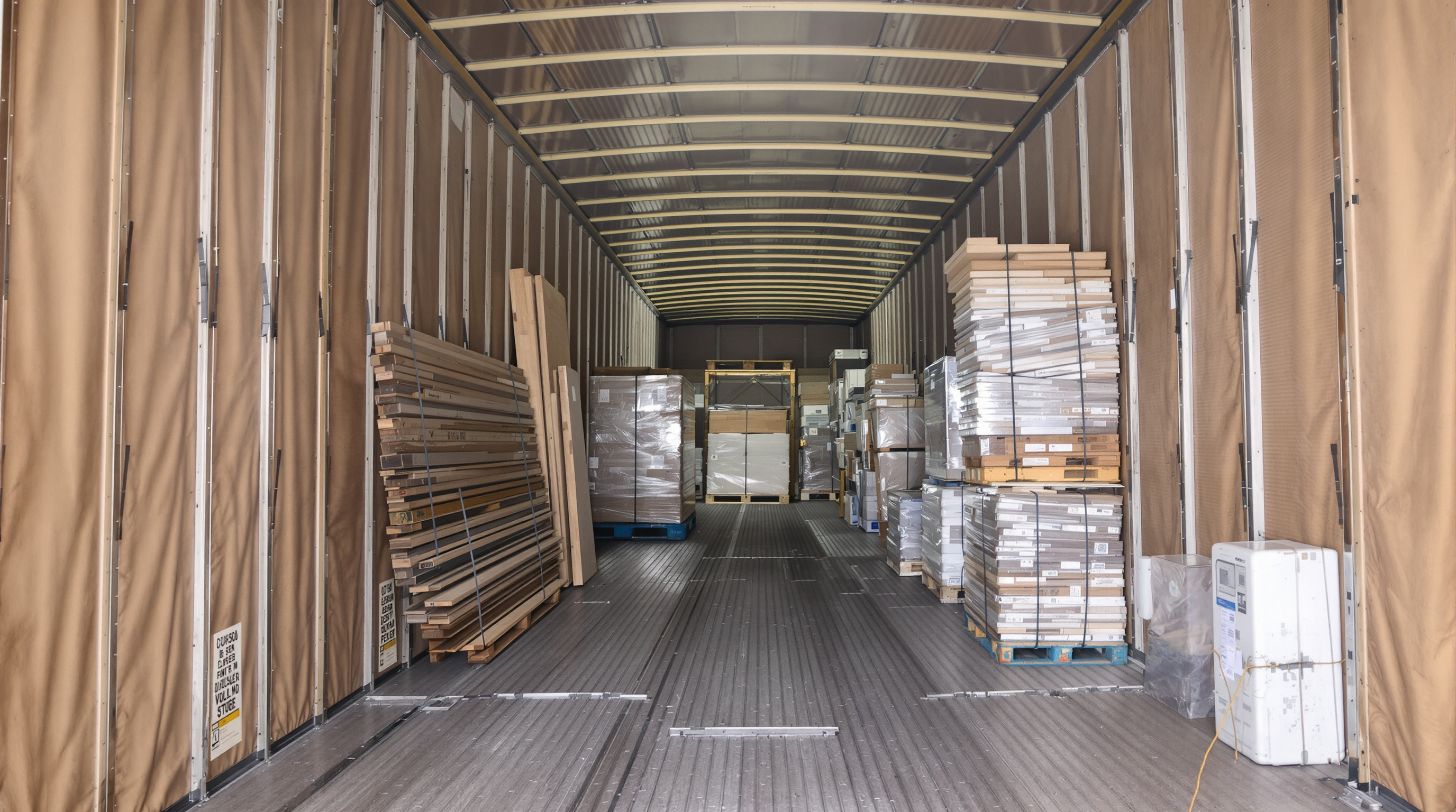 Interior of a curtain side trailer displaying lumber, drywall, and palletized goods with clear side access